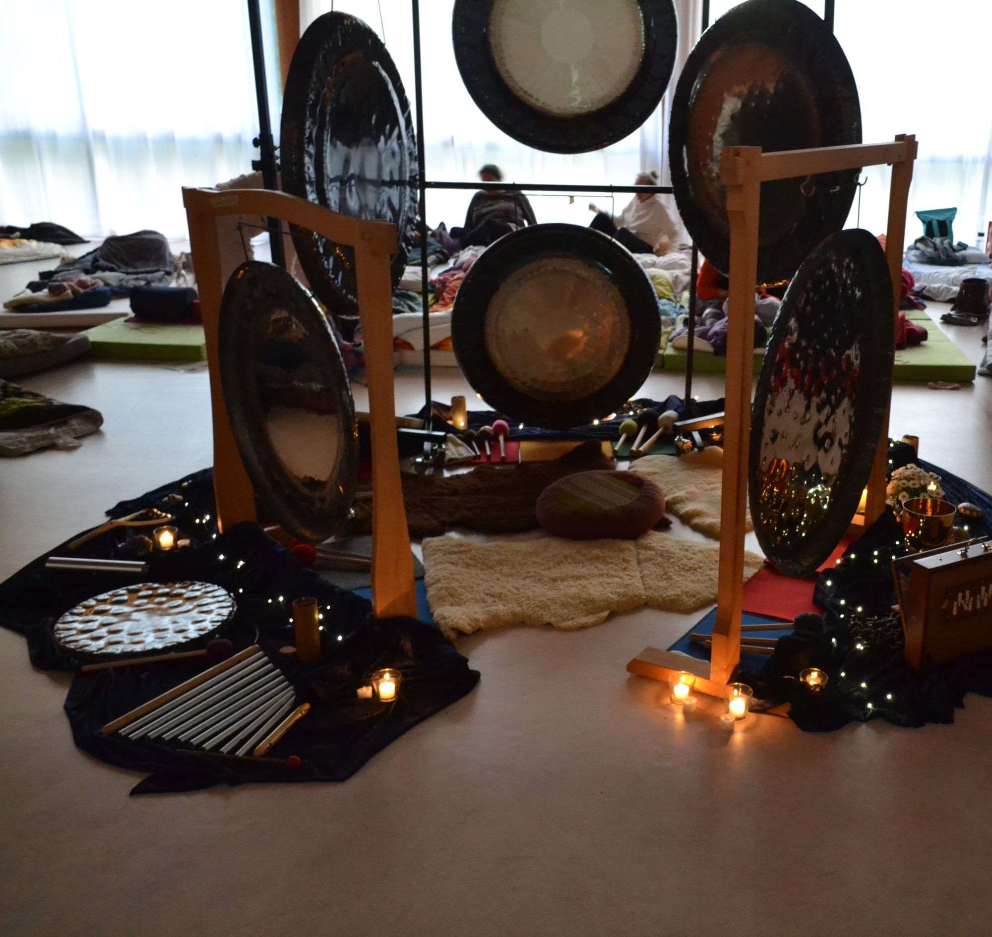Gongs auf Ständern, davor Kerzen und Lichterketten auf dem Boden, Symposium 2026