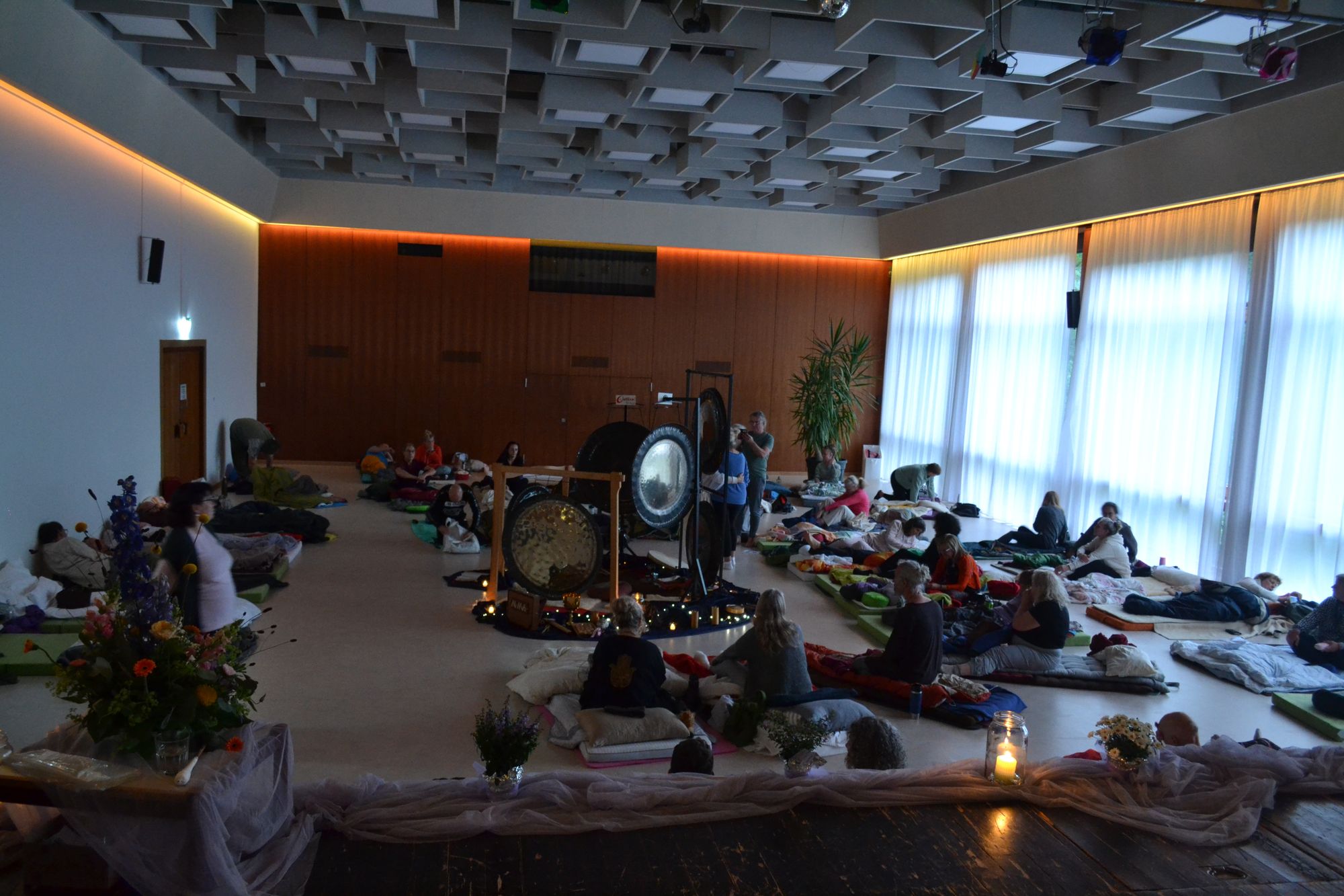 Ein Saal im Abendlicht, Menschen liegen auf Matten, im Hintergrund Gongs, Symposium 2026